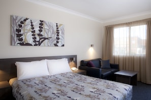 A hotel room with a large bed, a sofa, a small table, and a painting on the wall.