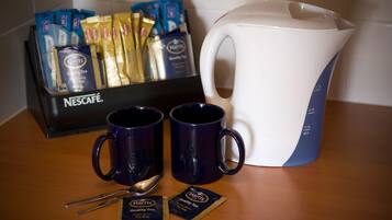 A coffee station with two blue mugs, a white and blue coffee pot, and a box of Nescafé coffee packets.