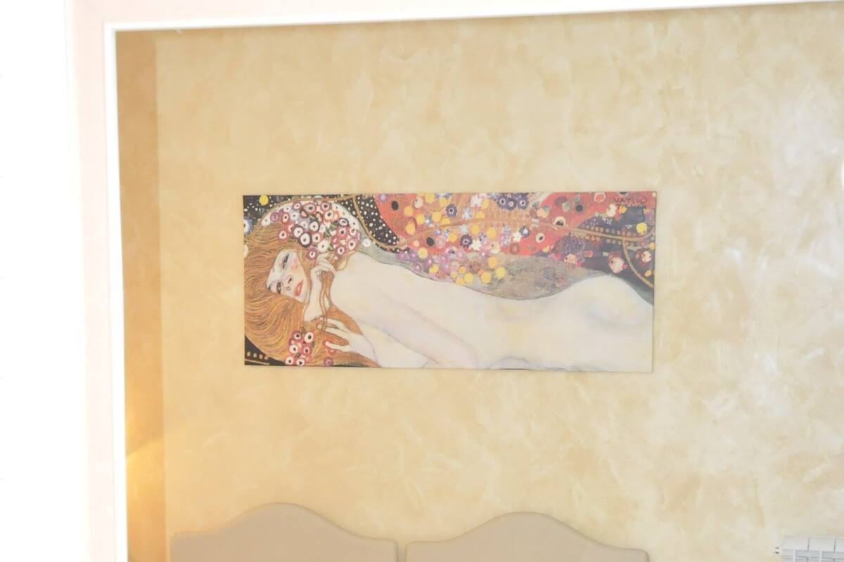 A hotel room with a bed, a painting on the wall, a desk with a computer, and a window.