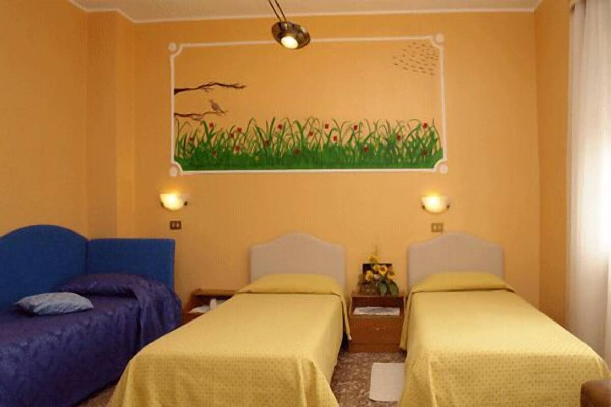 A hotel room with two beds, a painting of grass and birds on the wall, and two wall-mounted lamps.