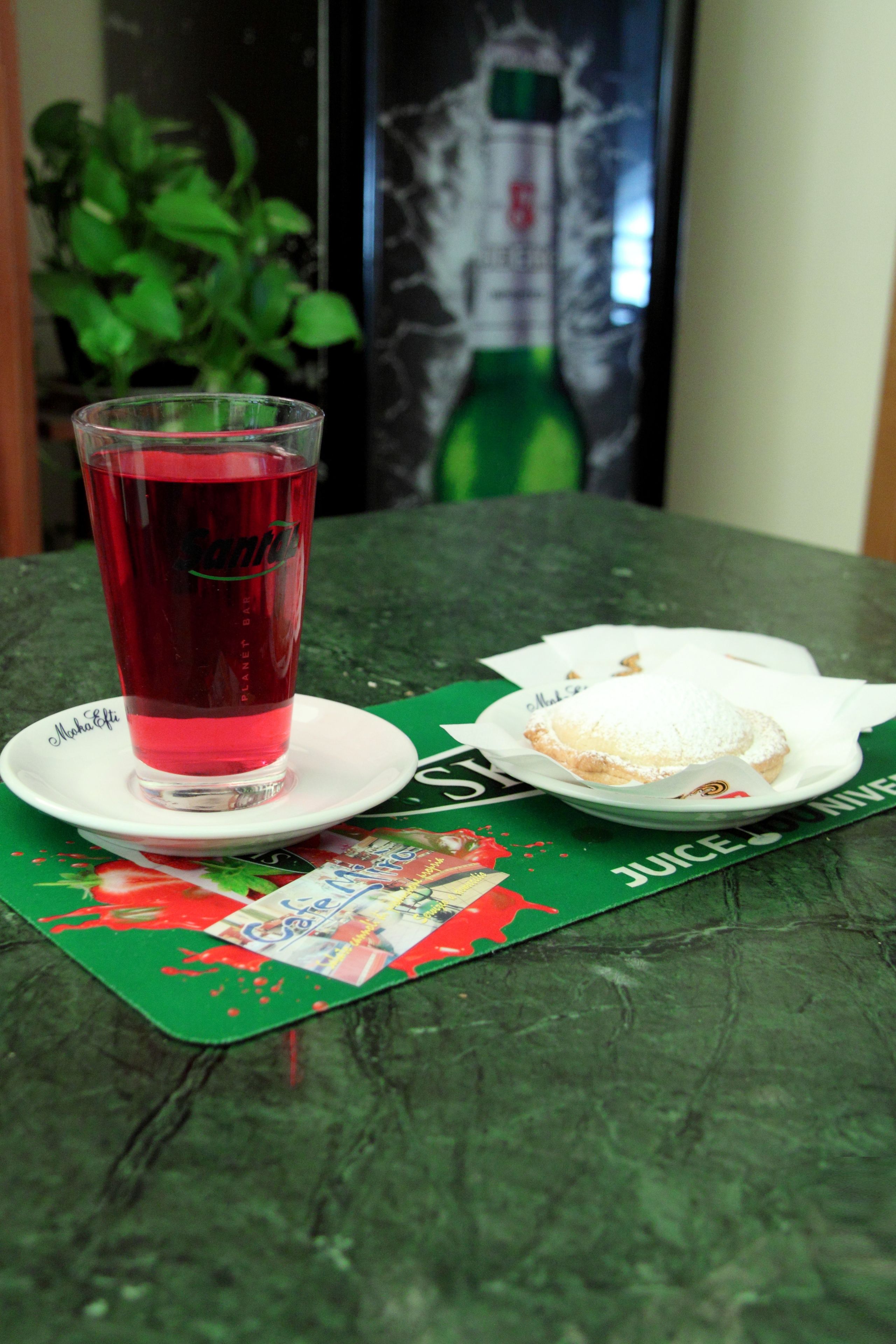 Una mesa con un vaso de bebida roja, un pastel y una base para platos verde con texto.
