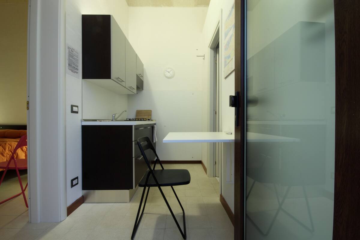 A compact kitchen with a black chair, a small countertop, and a white cabinet.