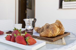 Een ontbijtsetting met aardbeien en croissants op een dienblad, een koffiepot en een witte beker op een tafel.