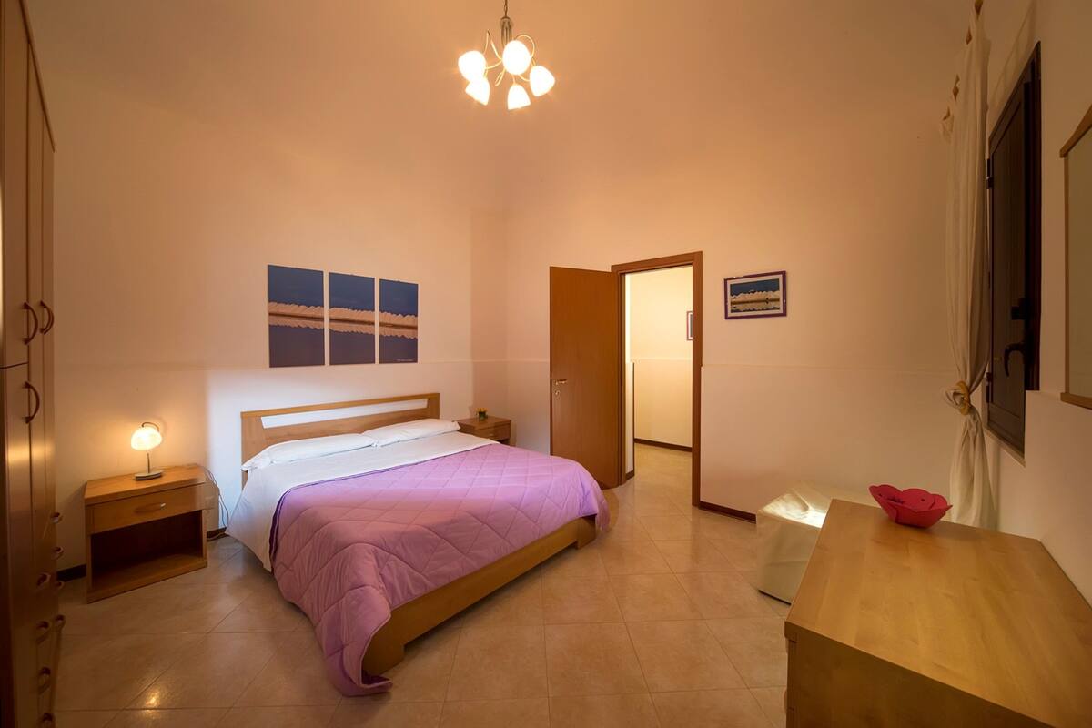 A bedroom with a bed, bedside tables, a wooden nightstand, a desk, and a chair.
