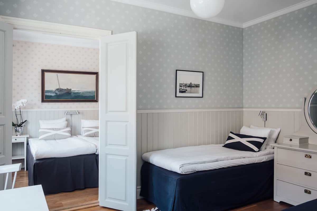 A bedroom with two beds, a white dresser, a bedside table, and a wall-mounted lamp.