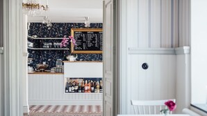 A bar area with a chalkboard menu, shelves with bottles, and a patterned rug. - Kivikstrand Badhotell (Kivik)