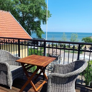 A balcony with wicker furniture and a wooden table, overlooking a body of water. - Kivikstrand Badhotell (Kivik)