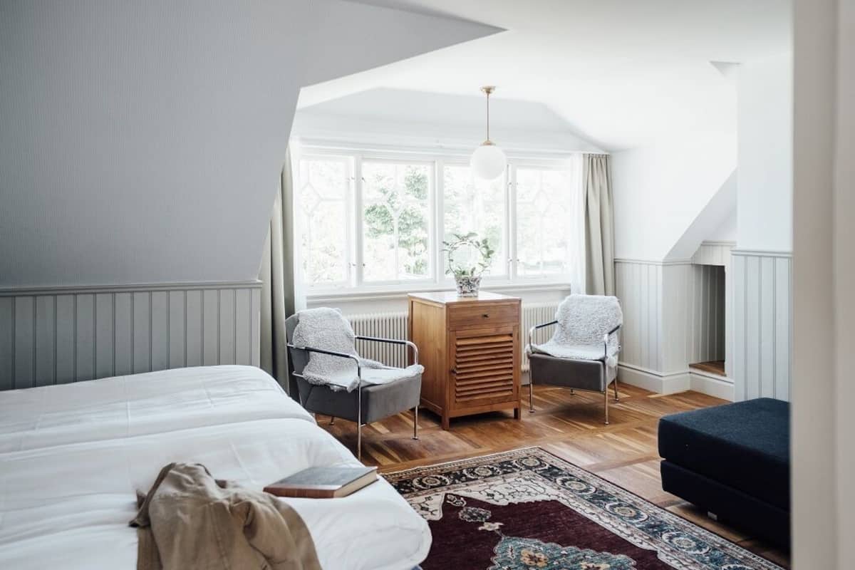 A bedroom with a large bed, two chairs, a dresser, and a window with curtains.