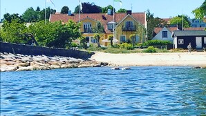 A coastal building with a red-tiled roof, a balcony, and a flag. - Kivikstrand Badhotell (Kivik)
