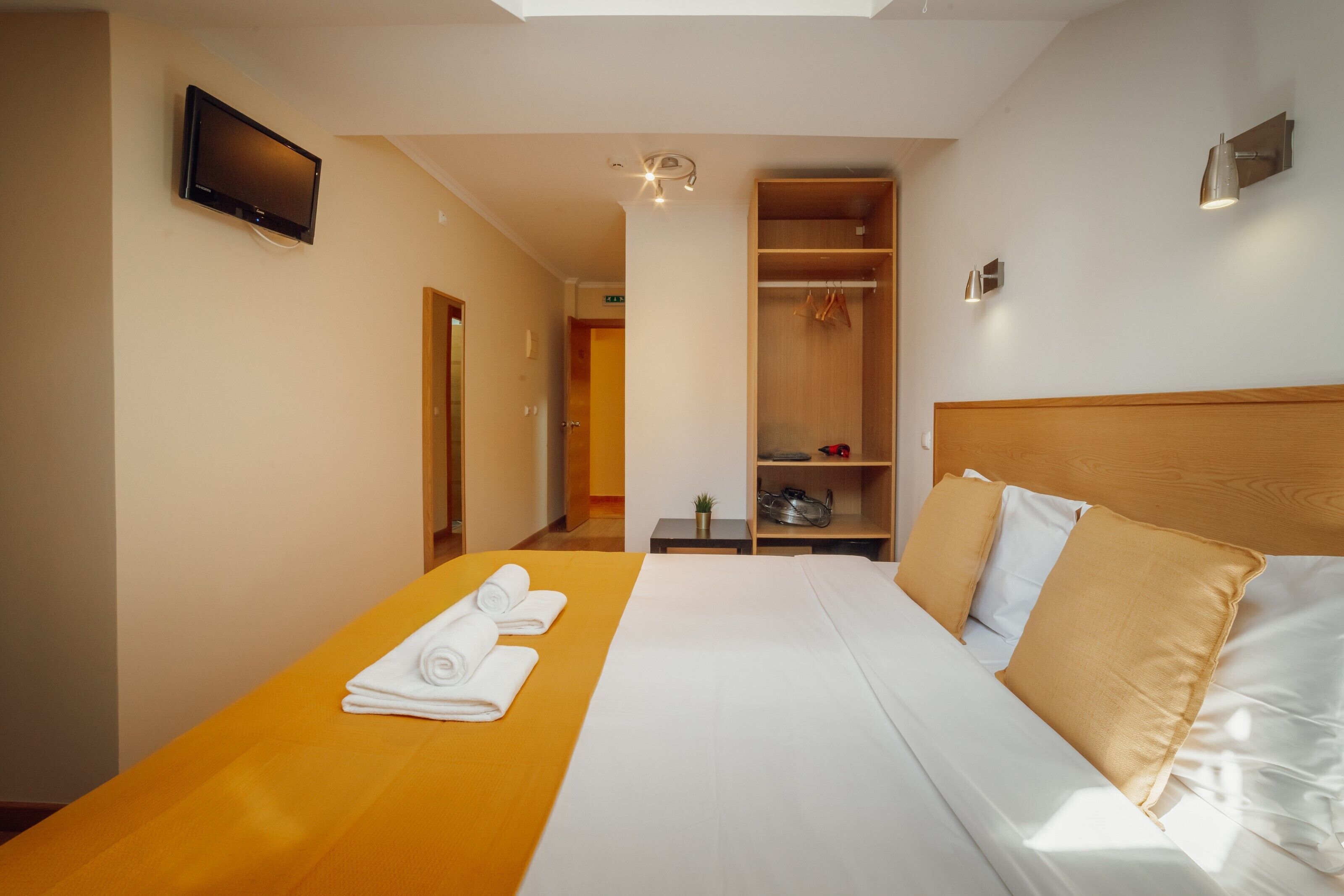 Une chambre d’hôtel avec un lit, un téléviseur fixé au mur, une armoire et une petite table sur laquelle est posée une plante.