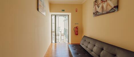 Un pasillo con un banco de cuero negro, un cuadro de bailarinas y un extintor en la pared.