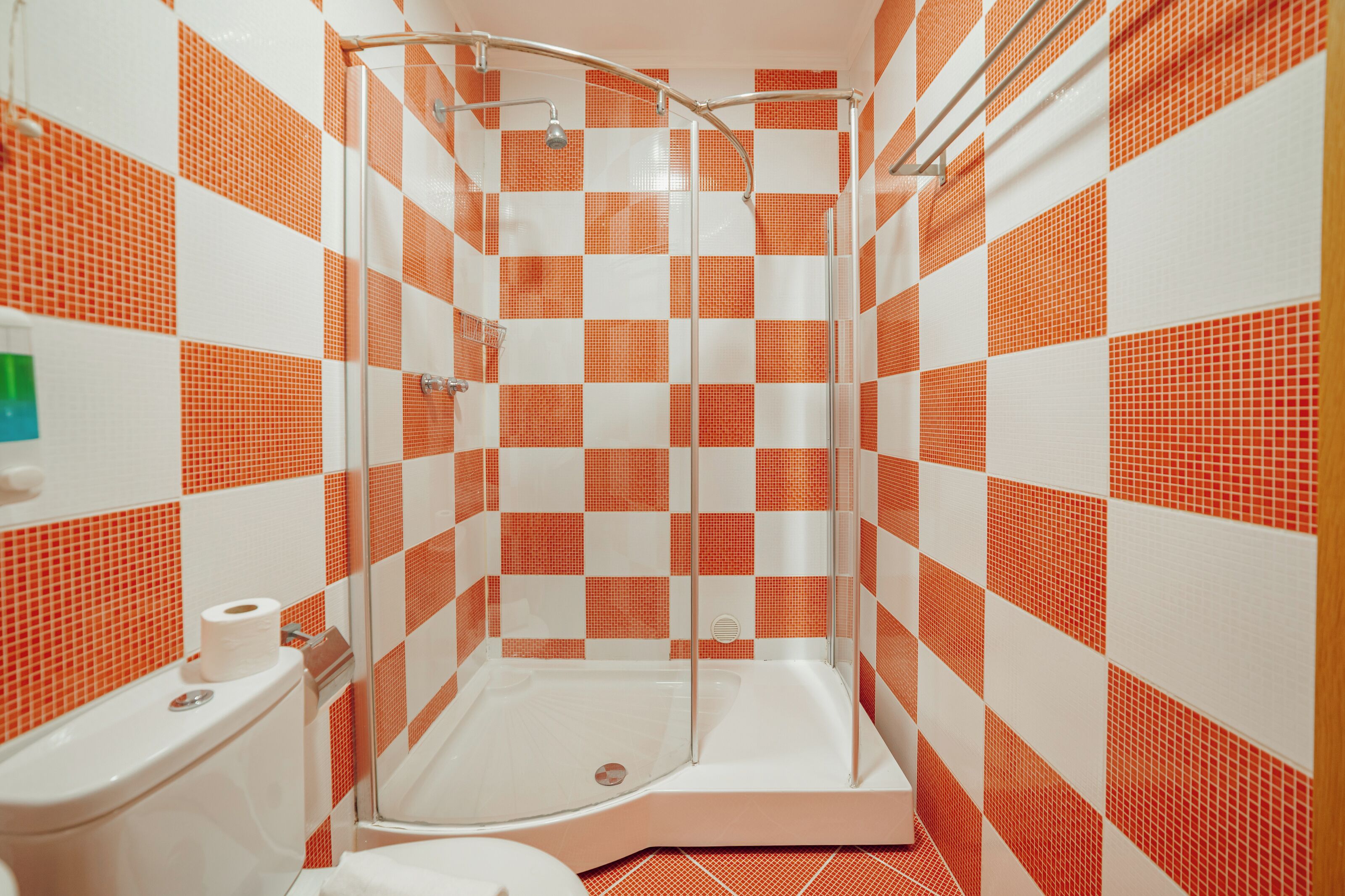 A shower stall with a glass door, a toilet, and a roll of toilet paper on the wall.