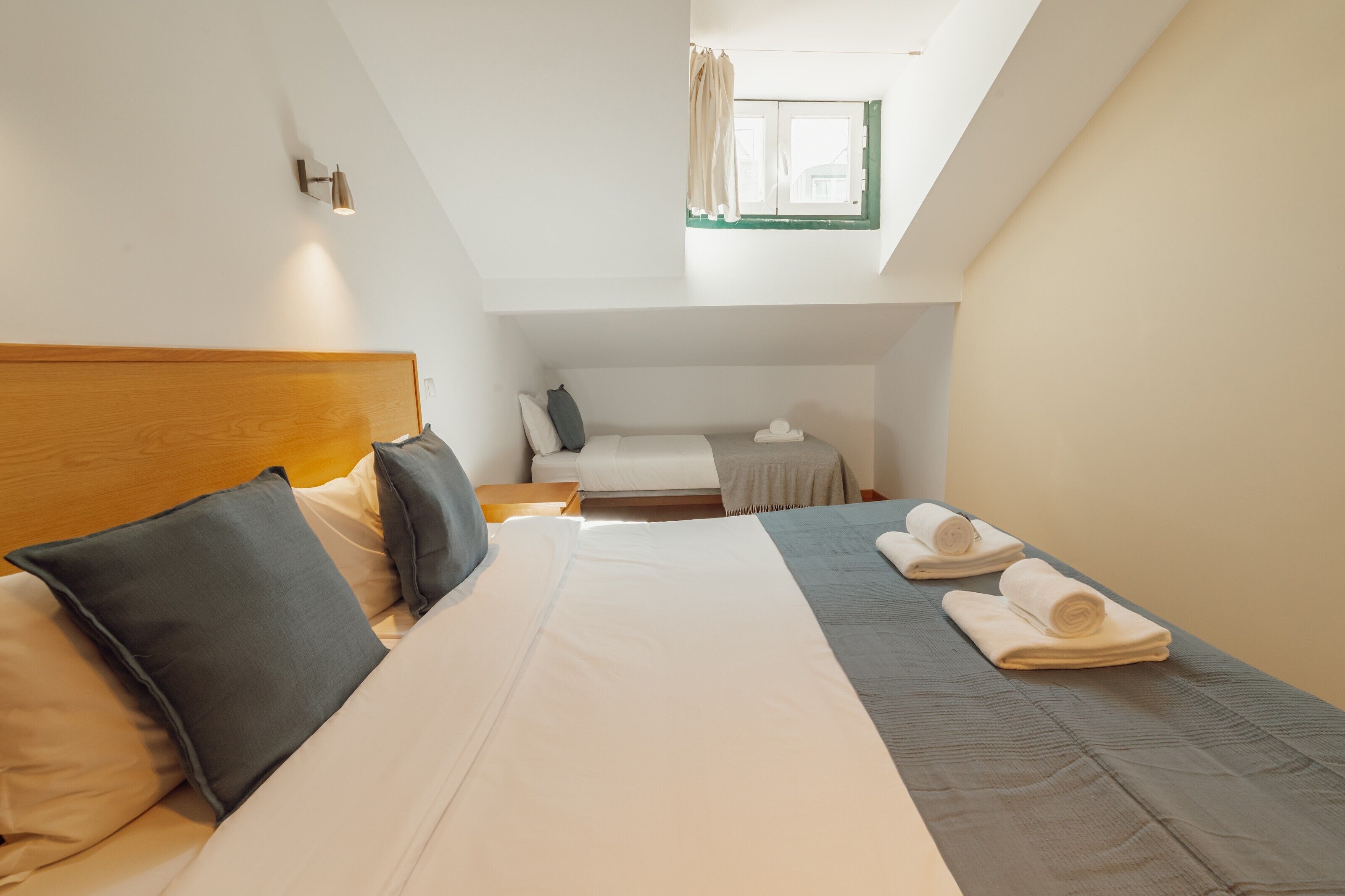 Een hotelkamer met een groot bed, een kleiner bed, een dakraam en een nachtkastje met een lamp.