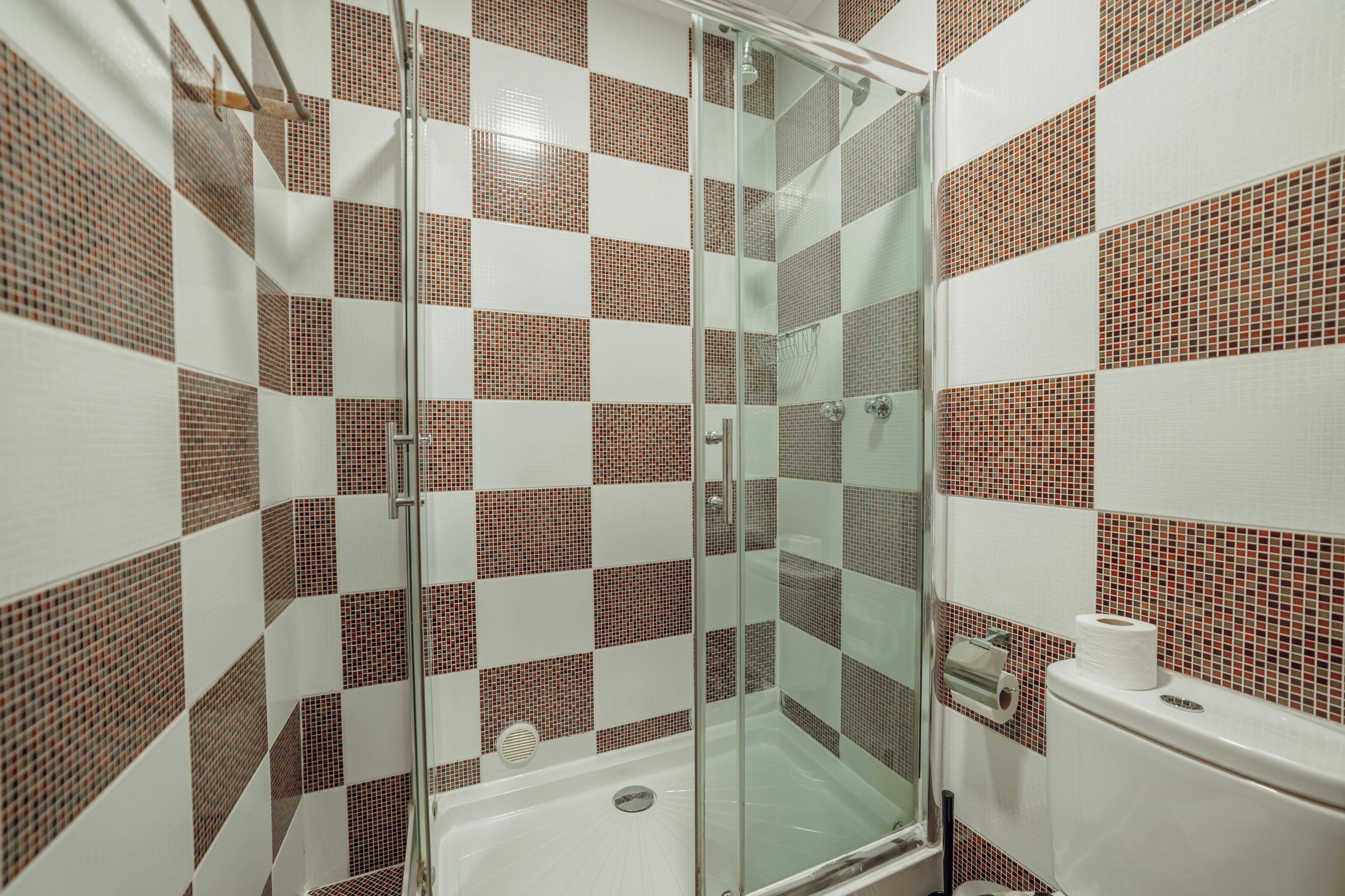 A bathroom with a glass shower enclosure, a toilet, and tiled walls.