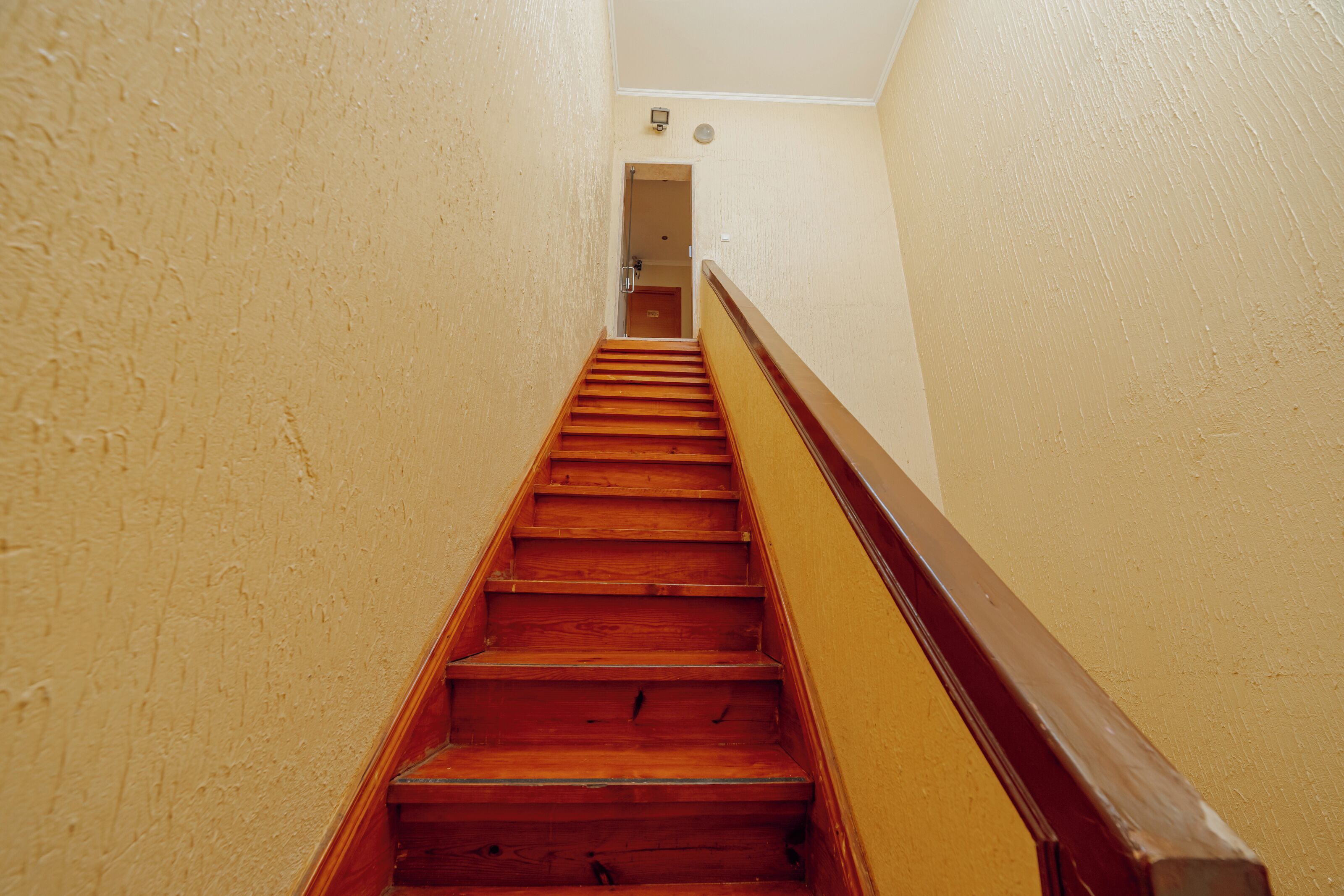 Een houten trap met een leuning, die leidt naar een deur aan de bovenkant.