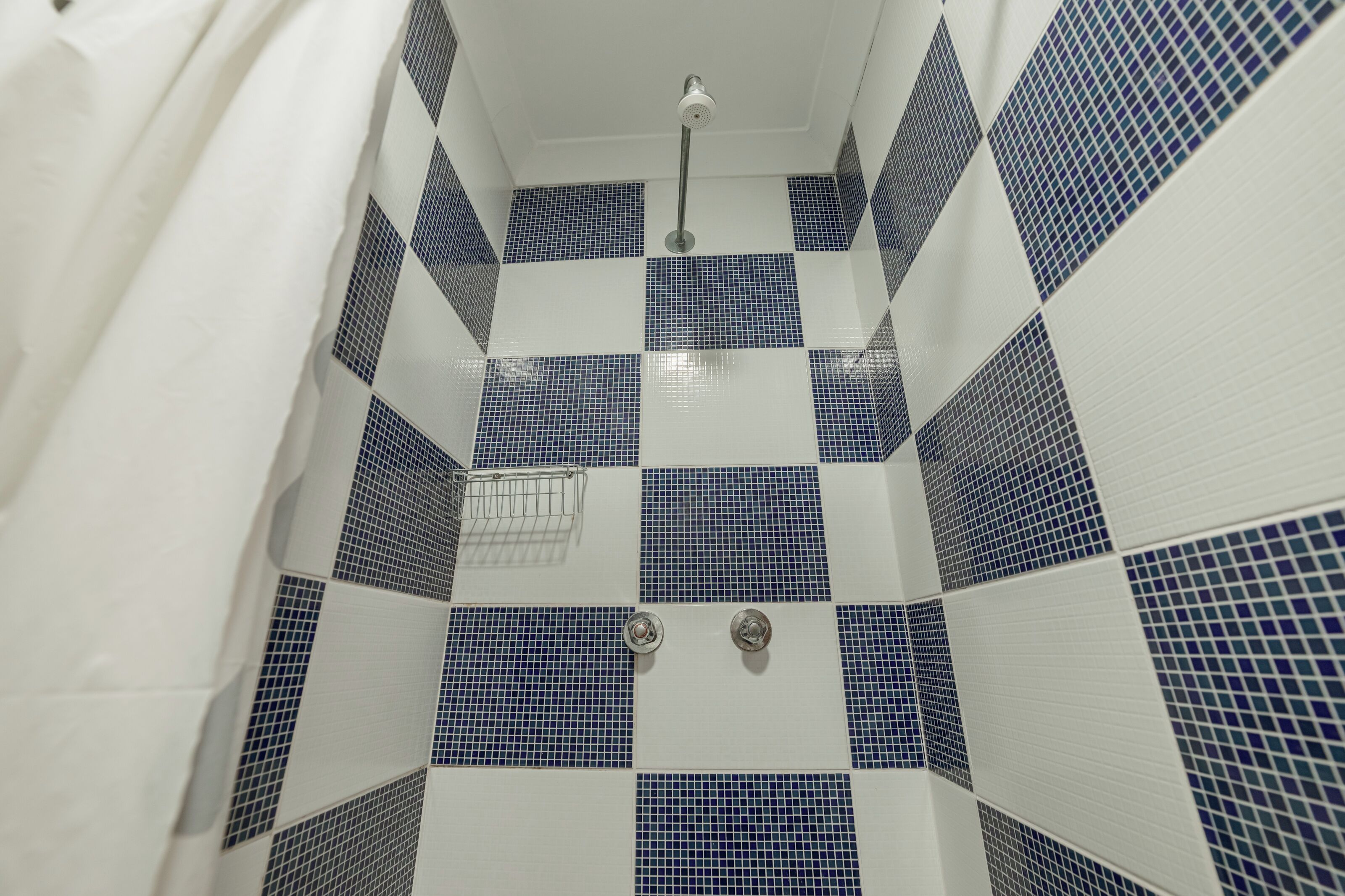 Un baño con baldosas azules y blancas a cuadros, un cabezal de ducha y un perchero.