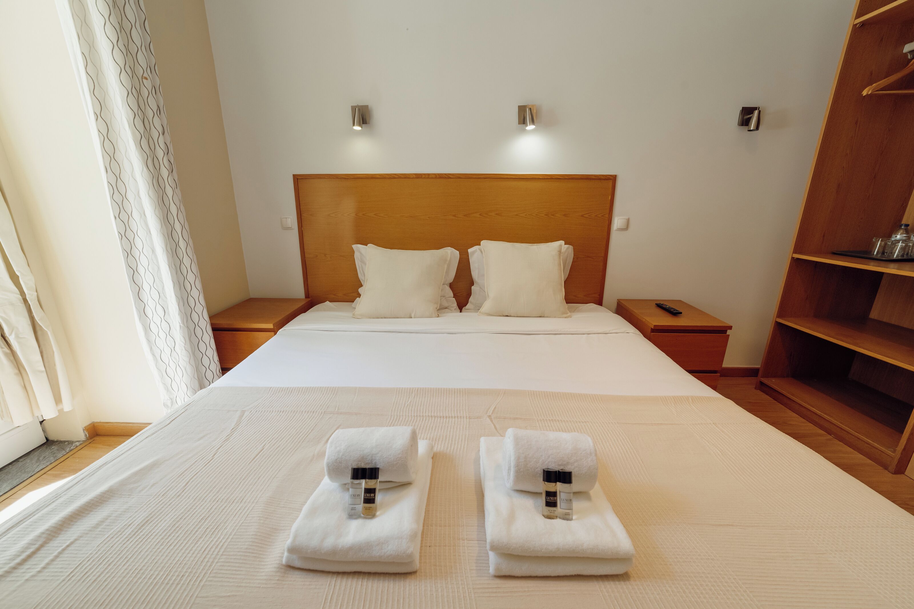 A neatly made bed with two pillows, a wooden headboard, bedside tables, and a wooden wardrobe.