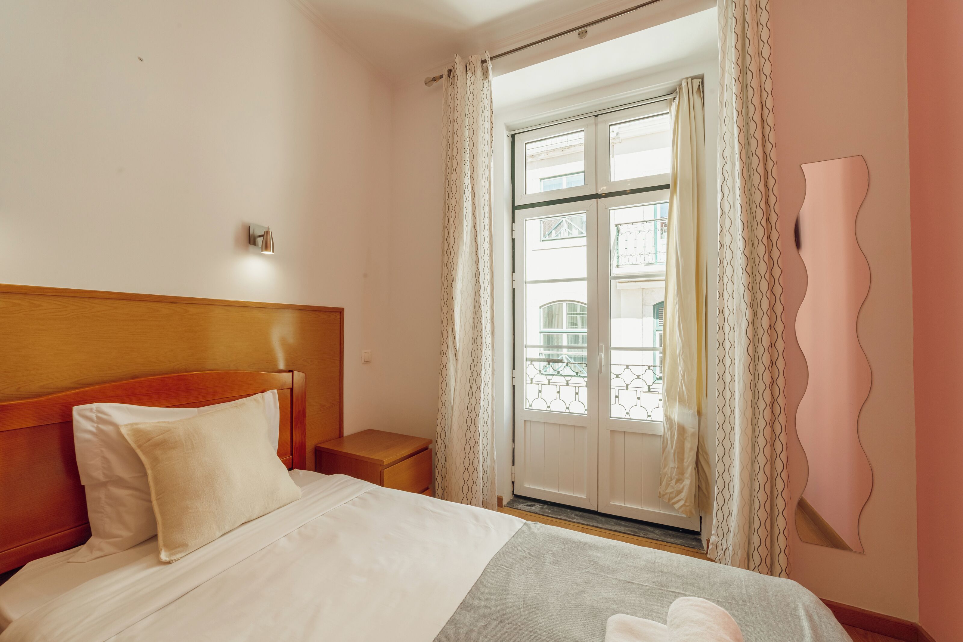 Une chambre d’hôtel avec une tête de lit en bois, un lit avec une literie blanche, une table de chevet, une fenêtre avec des rideaux et une vue sur l’extérieur.