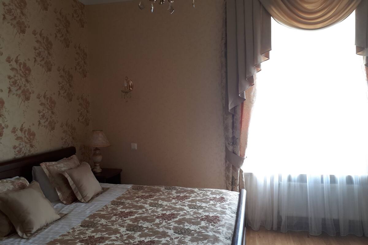 A bedroom with a bed, a nightstand, a lamp, and a window with curtains.