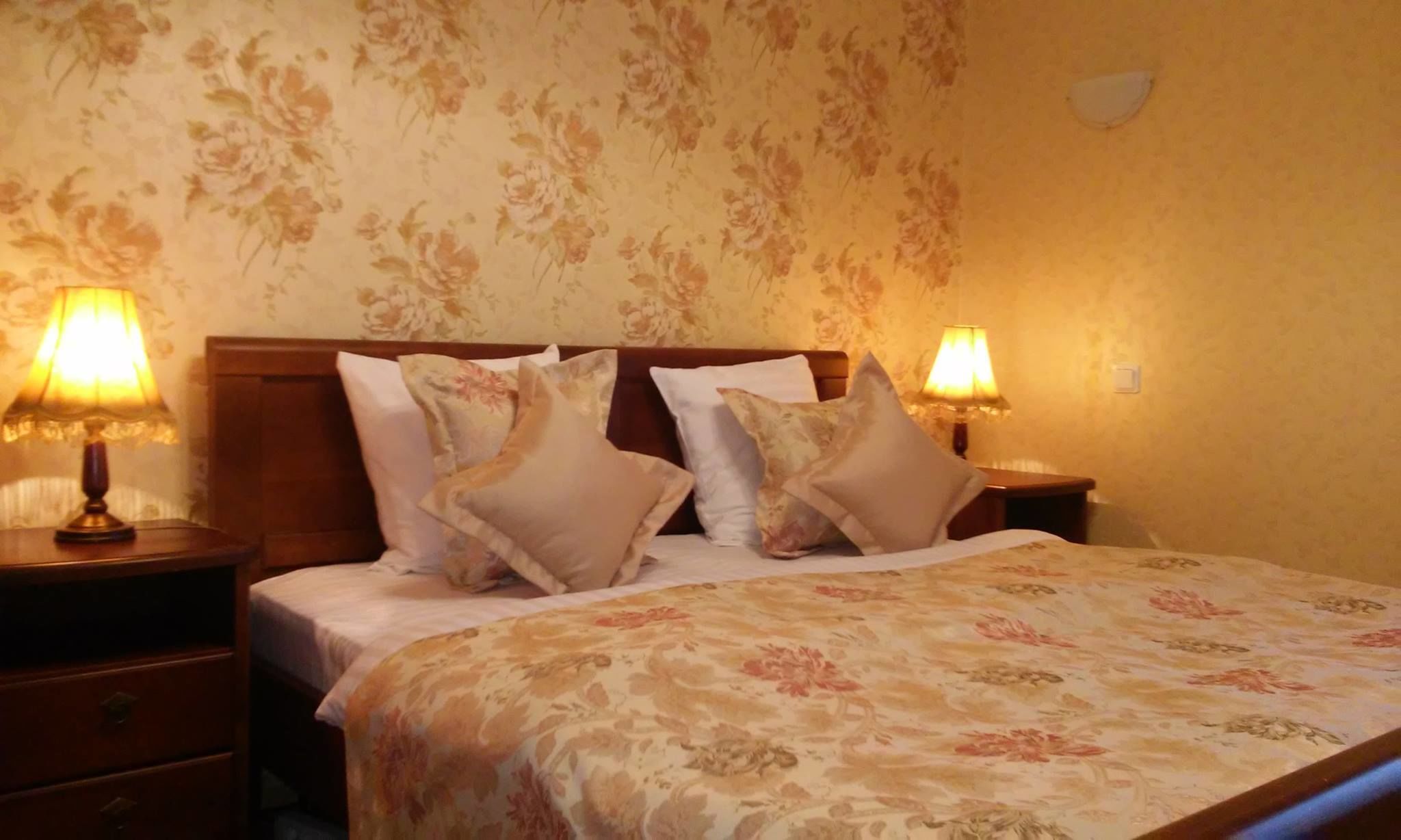 Un letto rifatto con biancheria da letto floreale, due lampade ai comodini e una parete decorata con motivi floreali.