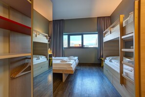 Une chambre d’hôtel avec des lits superposés, une grande fenêtre et un plancher en bois.