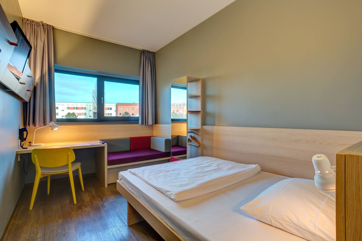 A modern hotel room with a bed, desk, and seating area.