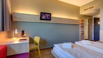 Ein Hotelzimmer mit Bett, Schreibtisch mit Lampe, Stuhl, Wandfernseher und Kleiderschrank.