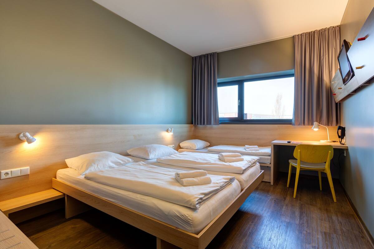 A hotel room with a large bed, a desk, a chair, and a TV mounted on the wall.