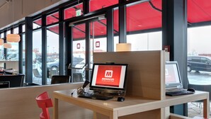 A modern workspace with two computer monitors, a keyboard, and a headset on a wooden desk. - MEININGER Hotel Berlin Airport (Berlin)