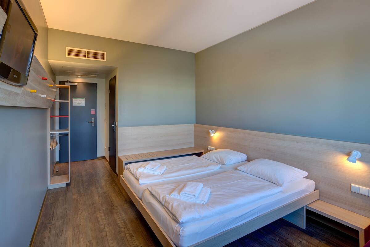 A hotel room with a bed, bedside tables, a TV, and a wardrobe.