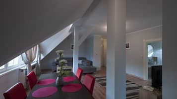 Een moderne woonkamer met een eethoek, met een donker houten tafel, rode stoelen en een grijze bank.