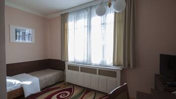 Una habitación pequeña con una cama individual, un radiador, un televisor y una ventana con cortinas.