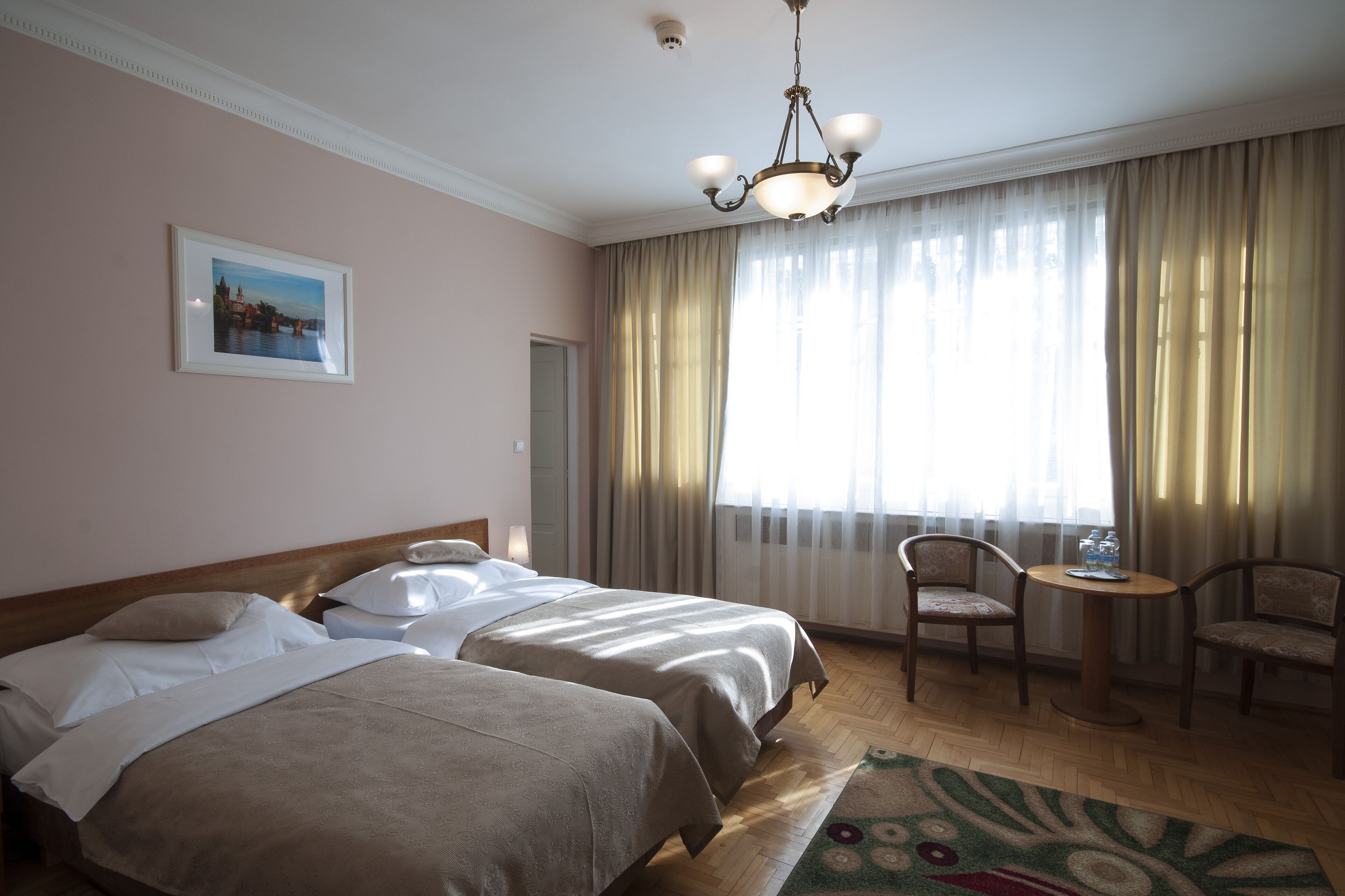 Ein Hotelzimmer mit zwei Betten, einem Chandelier, einem Wandbild und Blick ins Freie durch große Vorhänge.