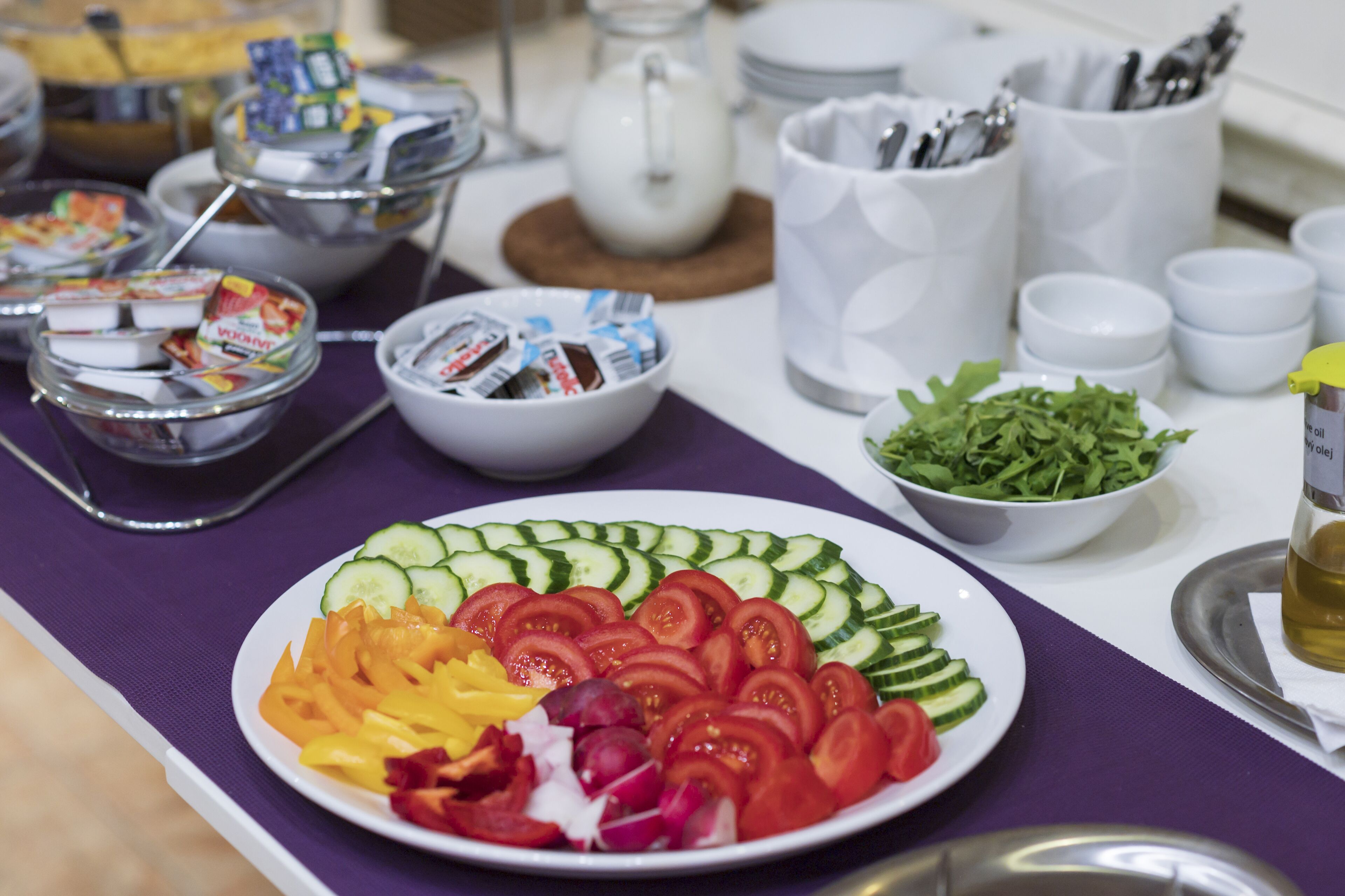 A buffet table with various food items including a plate of sliced vegetables and a bowl of salad.