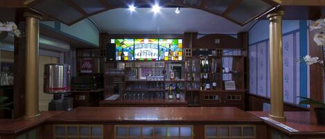 A bar area with a stained glass window, wooden bar counter, and shelves with bottles.