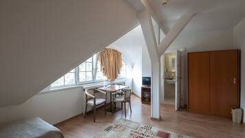A room with a sloped ceiling, a dining area with a table and chairs, a wardrobe, and a view through a window.