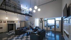 A spacious living area with a checkered floor, a fireplace, a staircase, and a balcony.