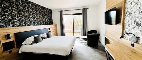 A modern hotel room with a large bed, a wooden headboard, a flat-screen TV, a desk, and a window with curtains.