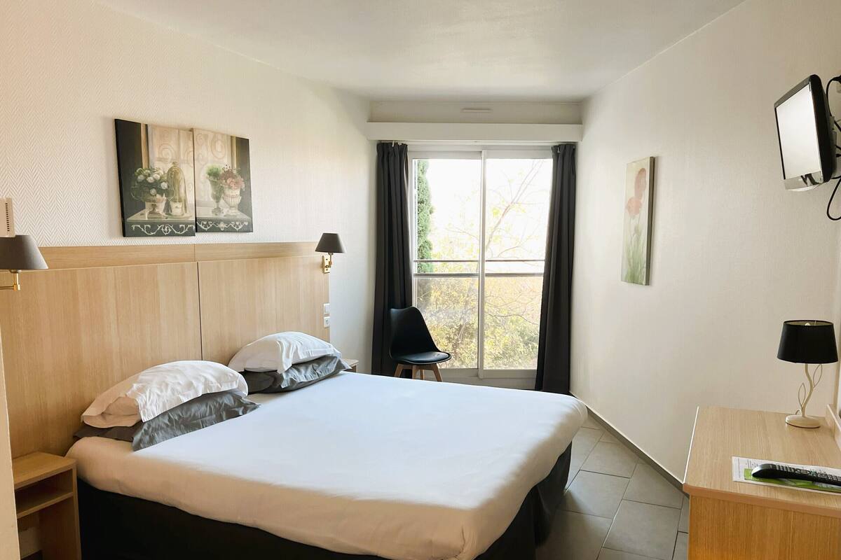 Une chambre d’hôtel avec un grand lit, un bureau avec un ordinateur, une chaise et une fenêtre avec des rideaux.