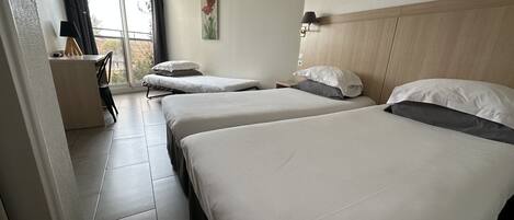 A hotel room with two beds, a desk, a chair, and a window with curtains.