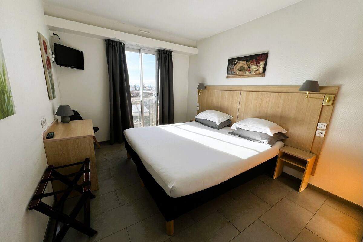 Une chambre d’hôtel avec un lit, un bureau, une chaise, une télévision, un tableau et une vue sur la ville.