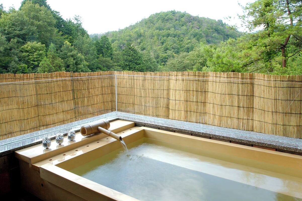 Un jacuzzi con cerca de bambú y vistas a una ladera boscosa.