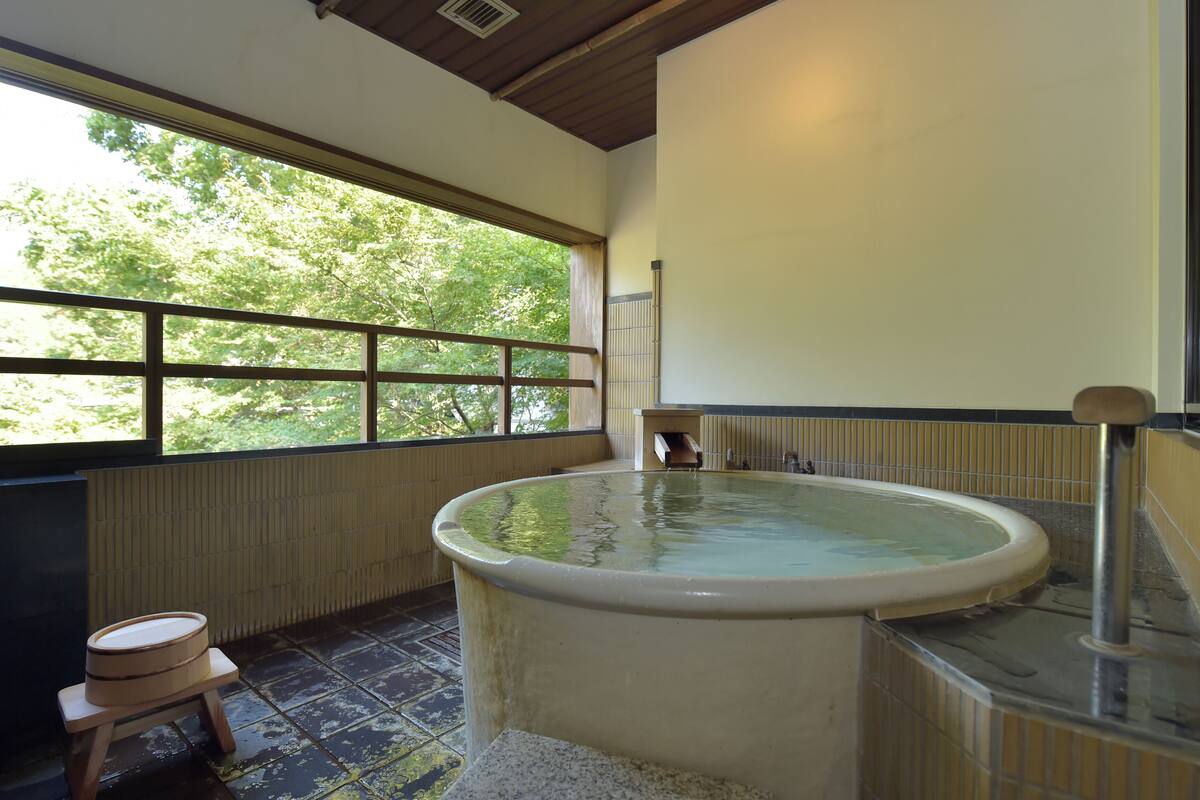 Una bañera de hidromasaje en una habitación con vistas a árboles a través de ventanas amplias.