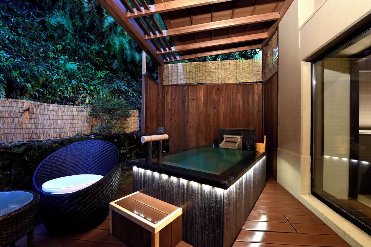 Un área de hidromasaje con una pérgola de madera, una silla de mimbre y una pequeña mesa.