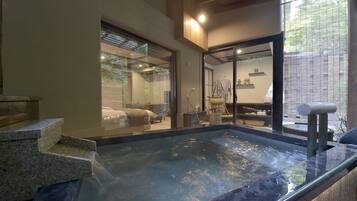 A hot tub area with steps leading into it, a glass door leading to a room with a bed, and a view of a garden outside.