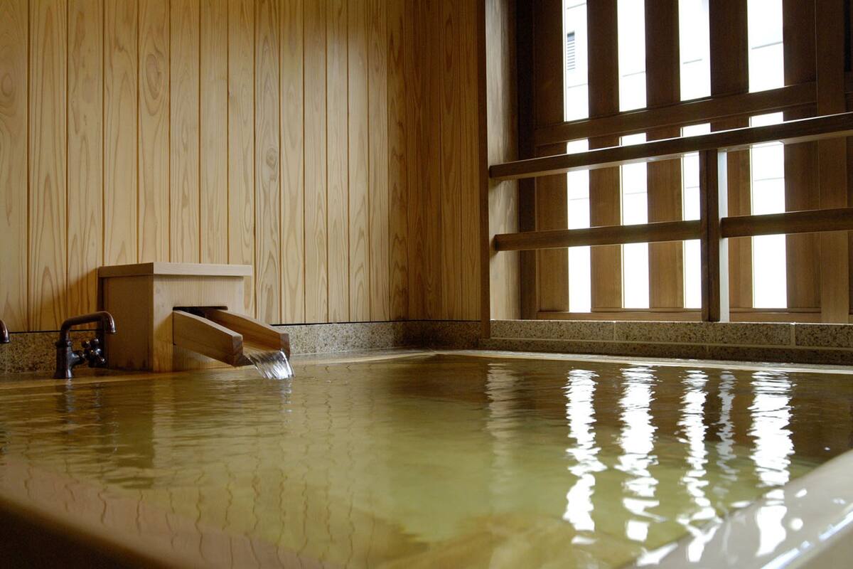 Interior de madera con una amplia piscina interior, un banco de madera y un ventanal con persianas verticales.
