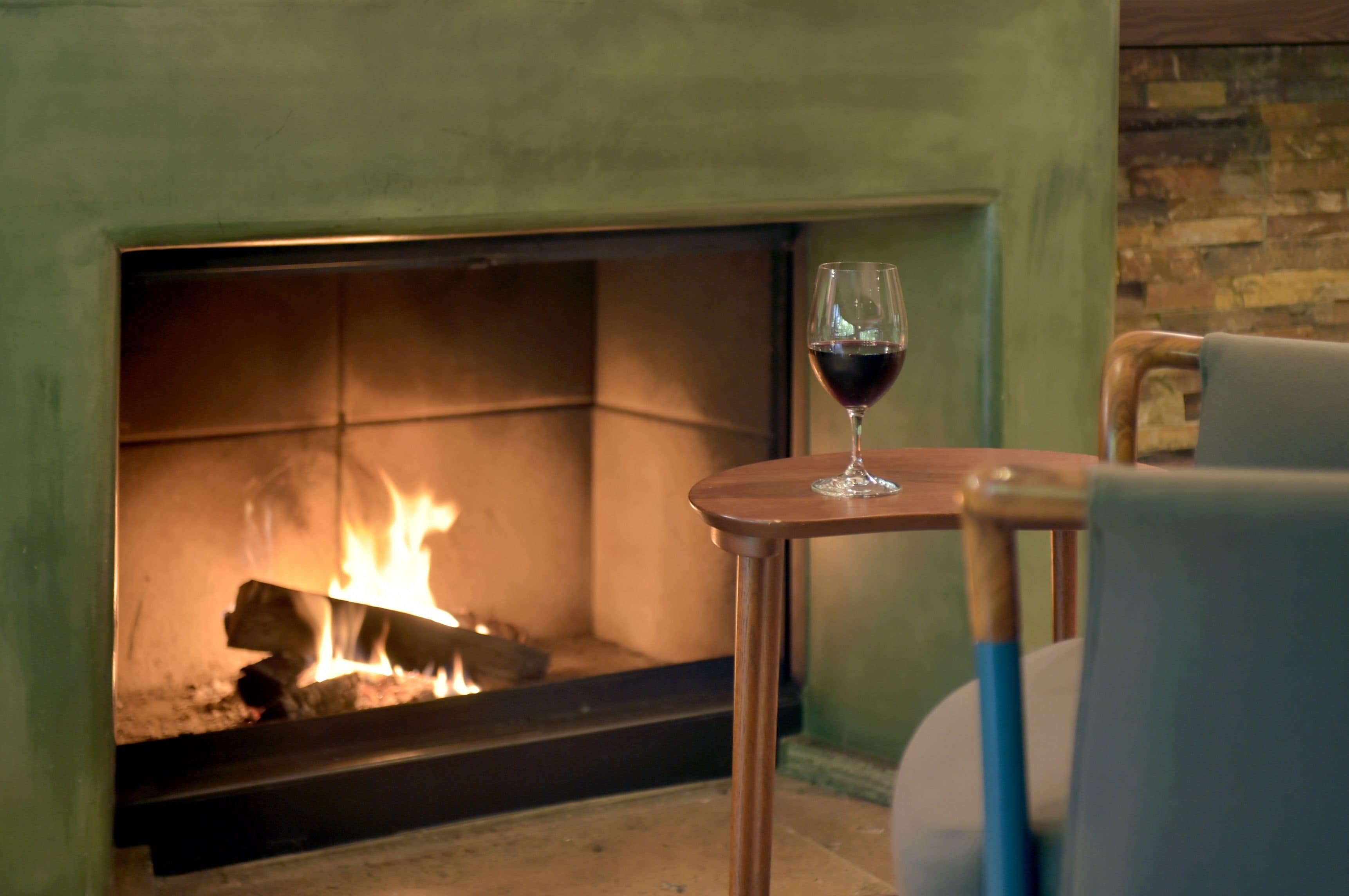 A fireplace with a glass of red wine on a small table.