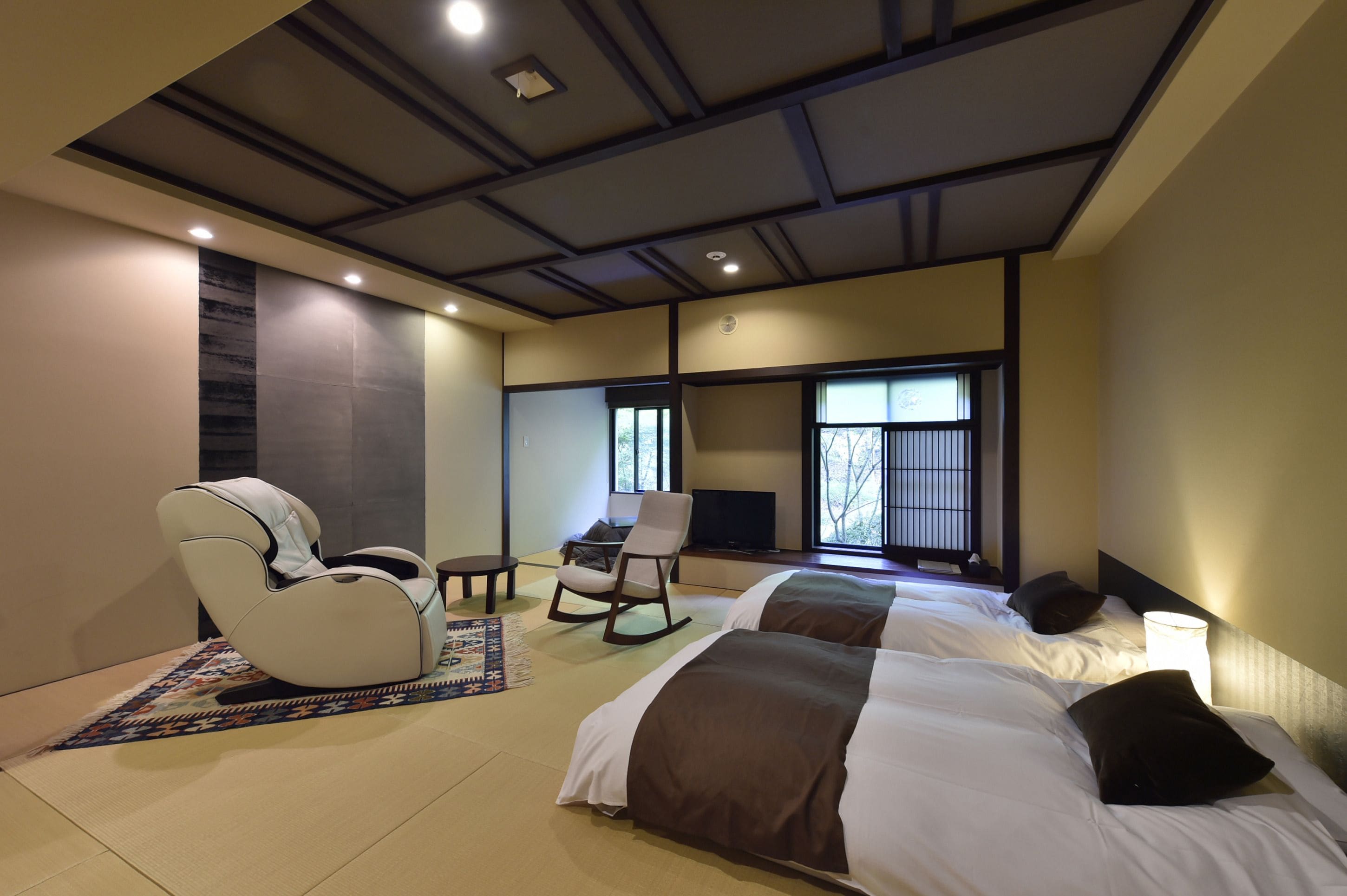 A modern hotel room with two beds, a massage chair, a desk, and a TV.