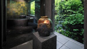 A bathroom with a stone sink, a large vase, and a view of lush greenery outside.