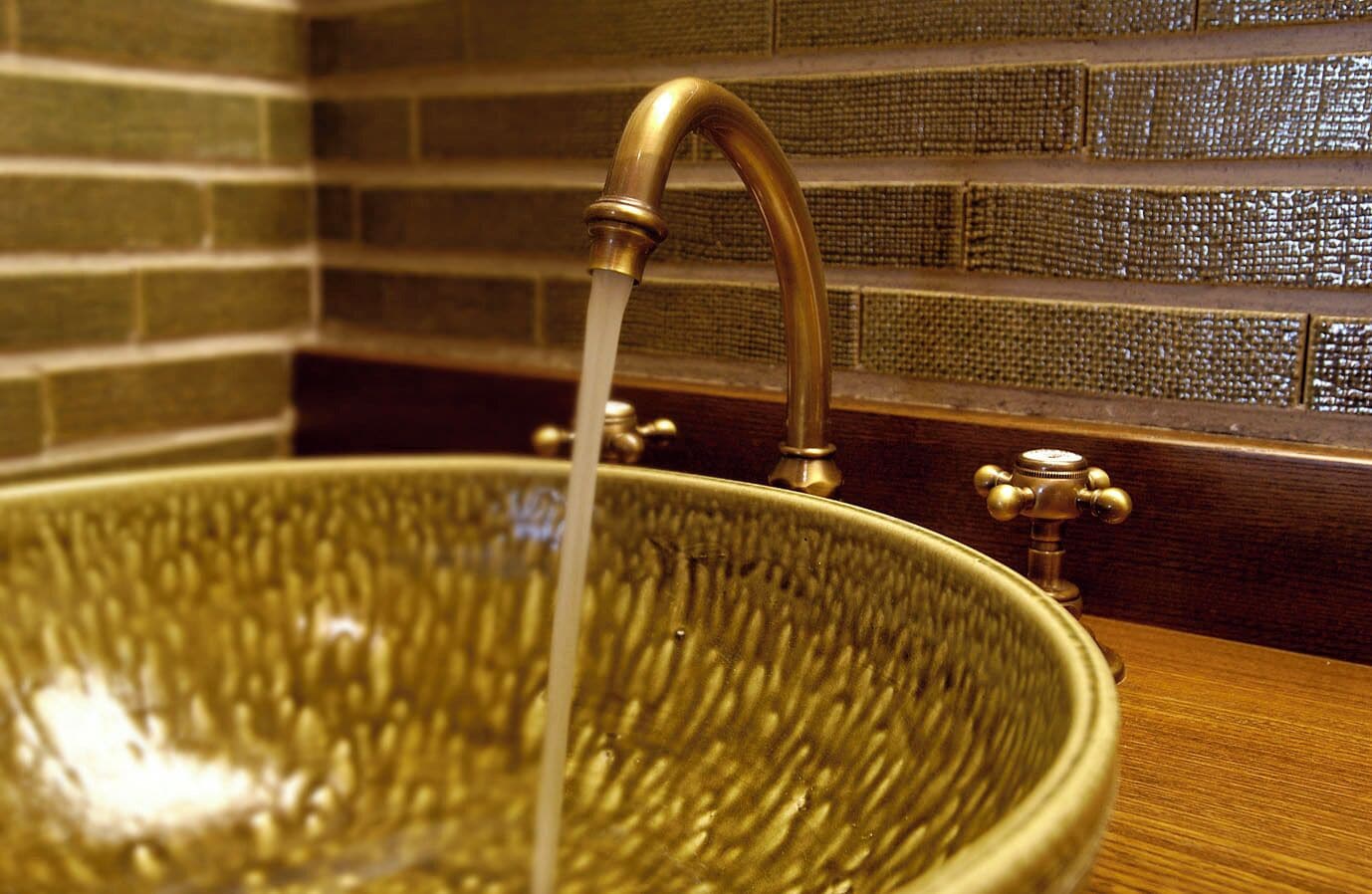 A large, ornate brass faucet with water flowing into a textured, bowl-shaped basin.